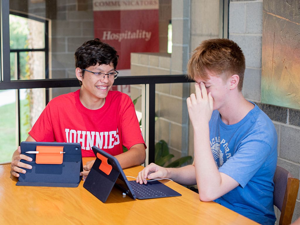 two students at a table with their tablets laughing